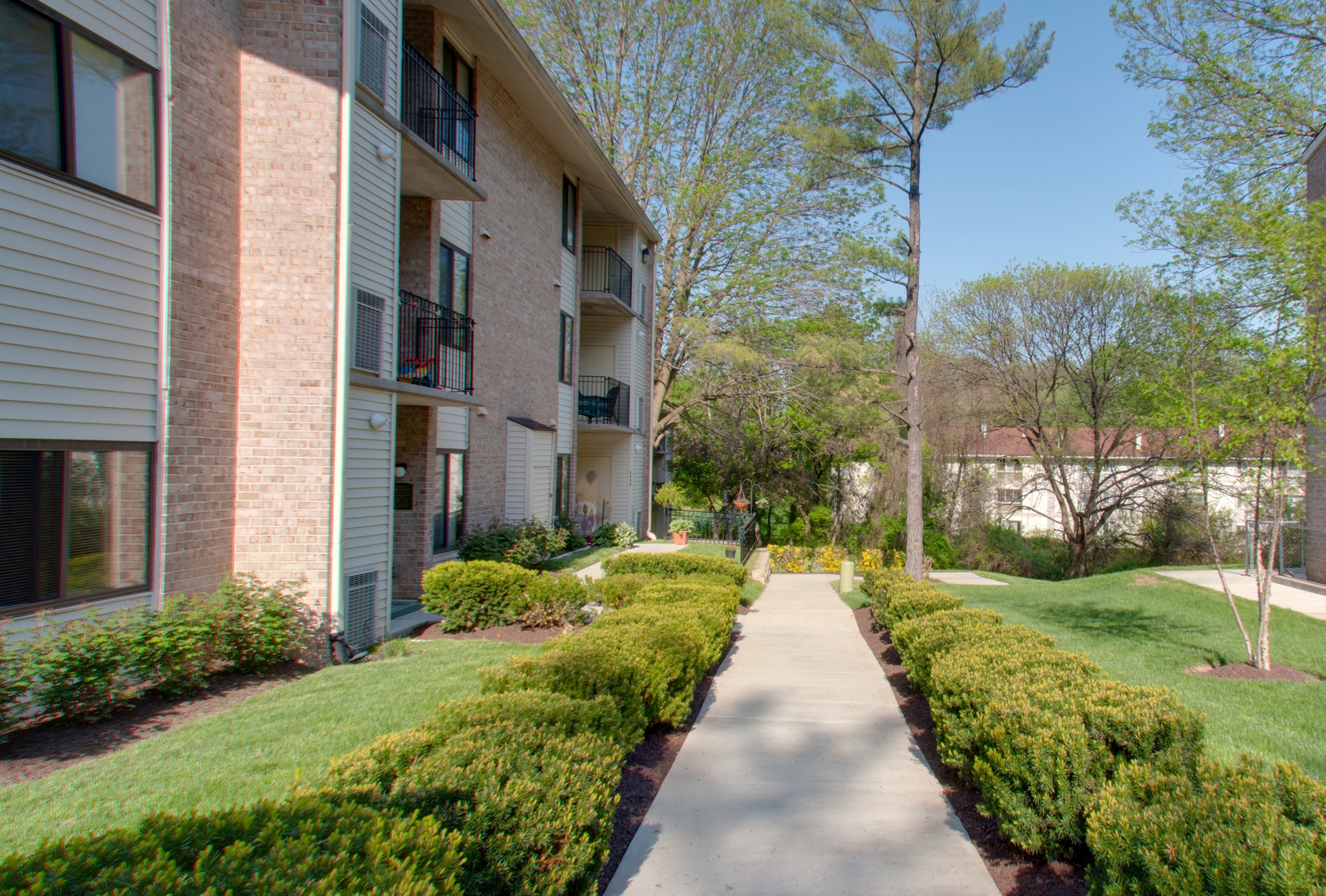 a sidewalk in front of an apartment building with grass and bushes