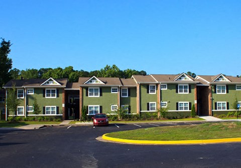 A red car is parked in the driveway of a green house.