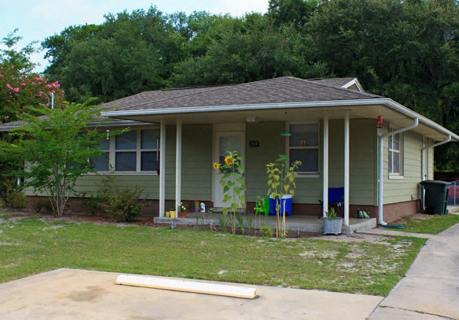 a small green house with a porch and some plants