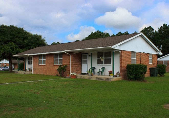 a brick house with a green lawn and a cloudy sky