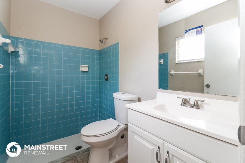 a blue tiled bathroom with a toilet sink and mirror