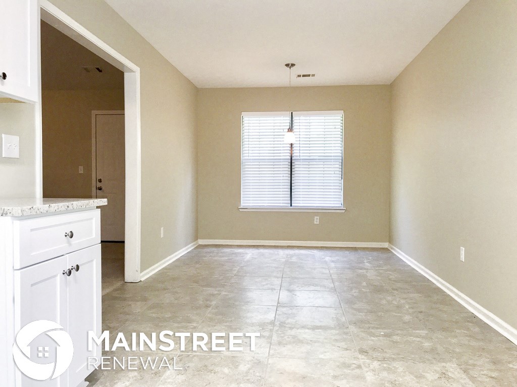 an empty kitchen and dining room with a window and white cabinets