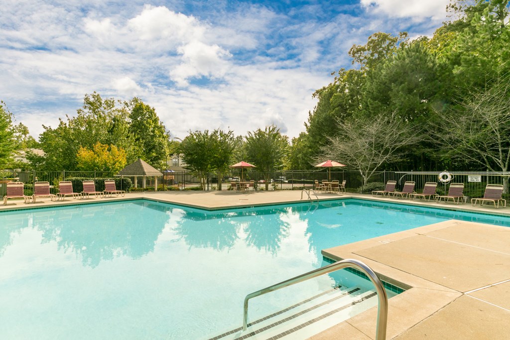 a swimming pool with chairs and trees in the background