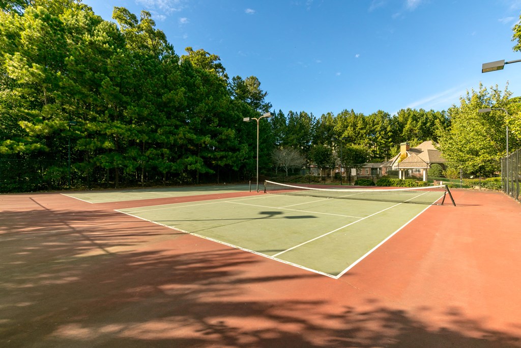 a tennis court with a house and trees in the background