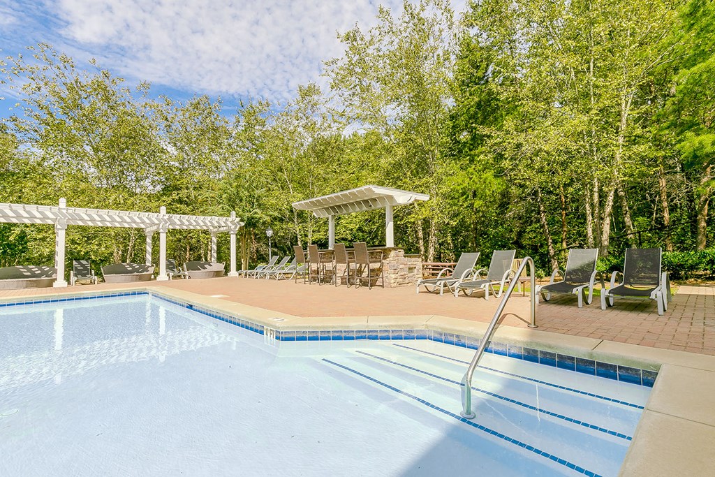 a swimming pool with chairs around it and trees in the background