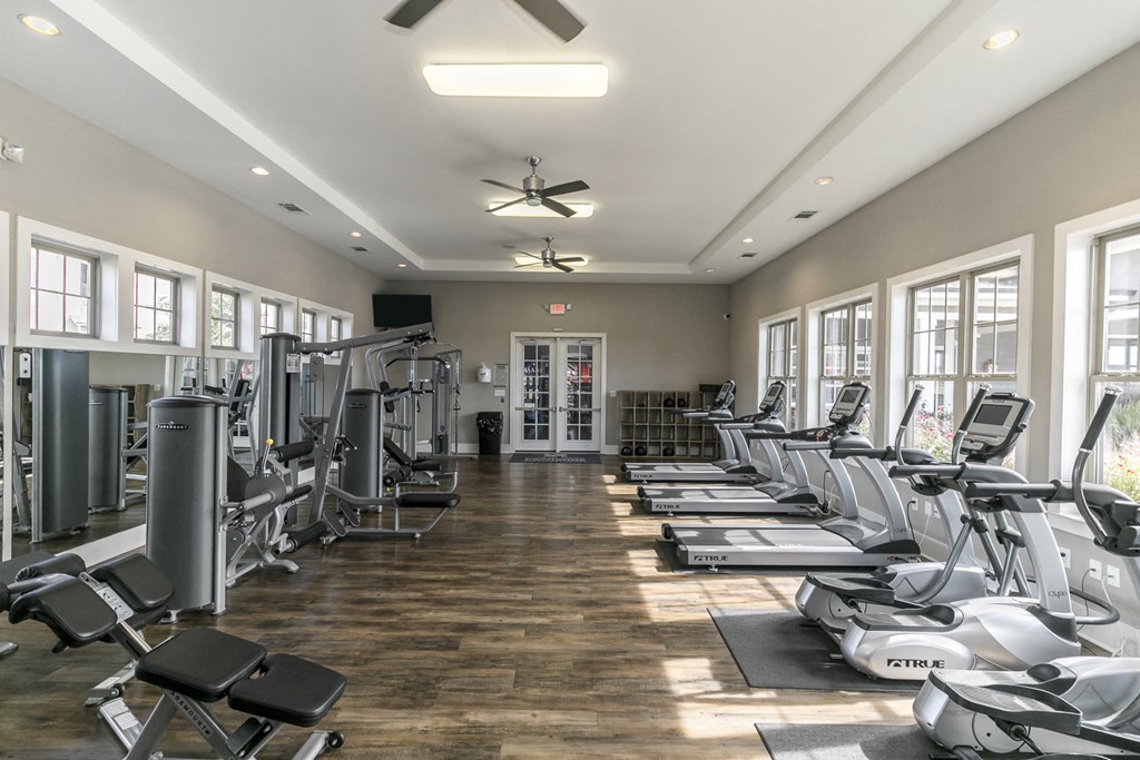 a gym with cardio machines and chairs and windows