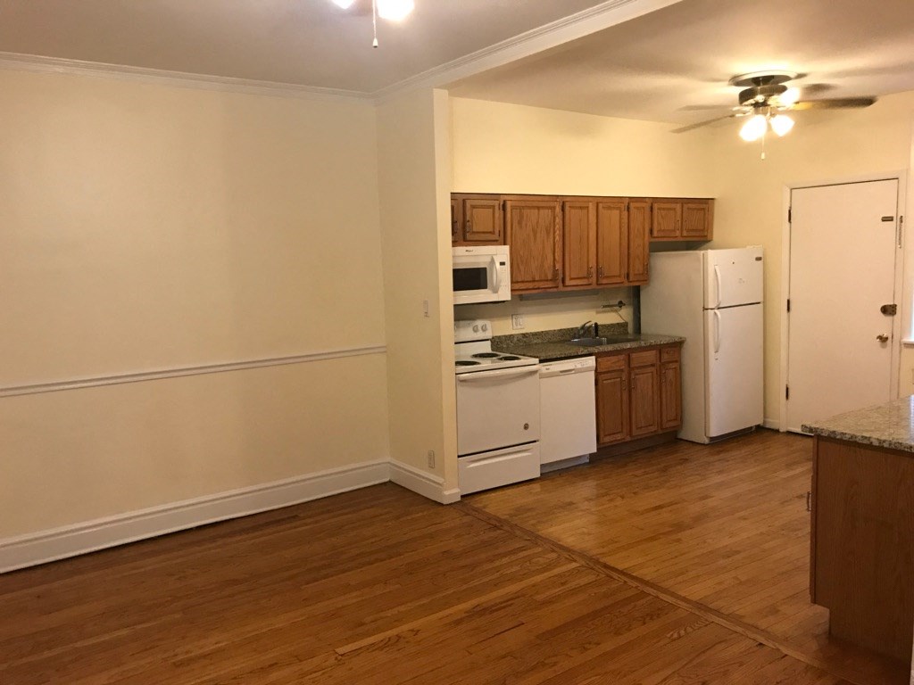 an empty kitchen with white appliances and wooden floors
