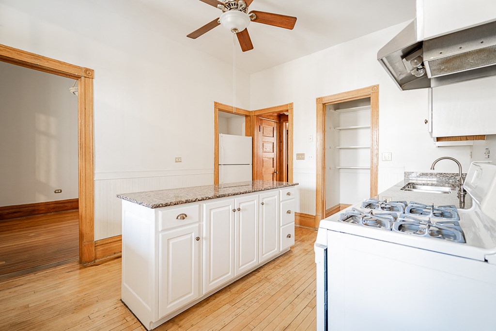 a kitchen with white cabinets and a stove and a ceiling fan