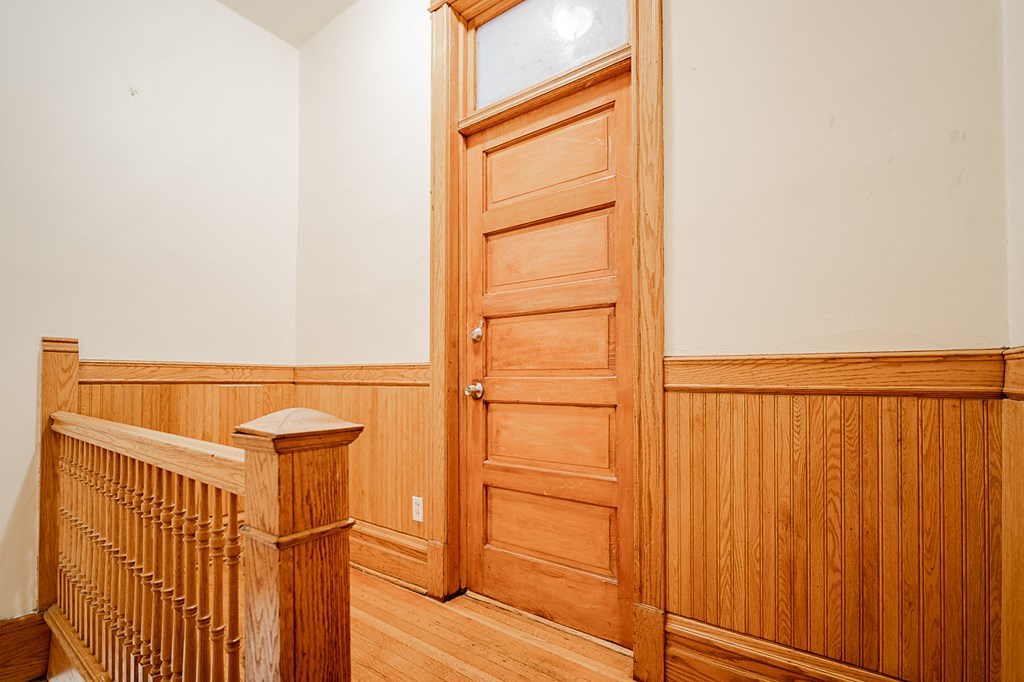 a hallway with a wooden door and a staircase with a window