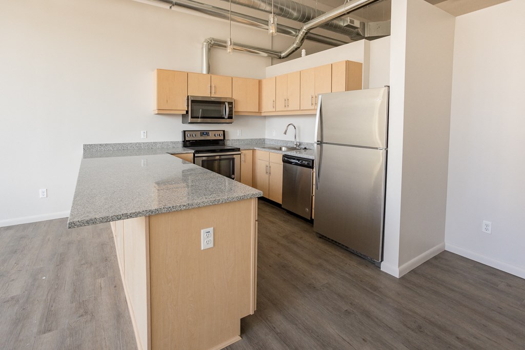 A kitchen with a stove top oven, microwave, refrigerator, and wooden cabinets.