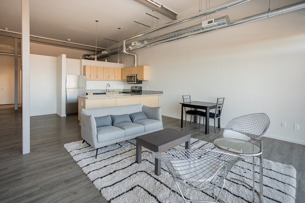 A modern living room with a grey sofa, a glass table, and a striped rug.
