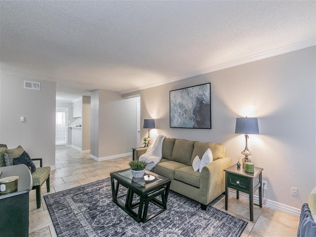 Open-concept living room with neutral tones and tile floors at Riata Park Apartments