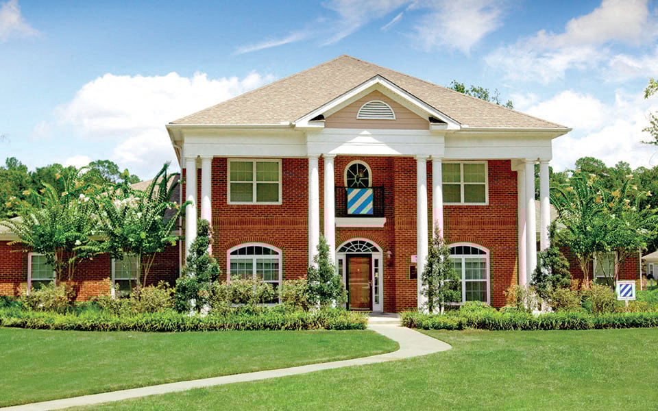 the front facade of a brick house with a lawn and trees