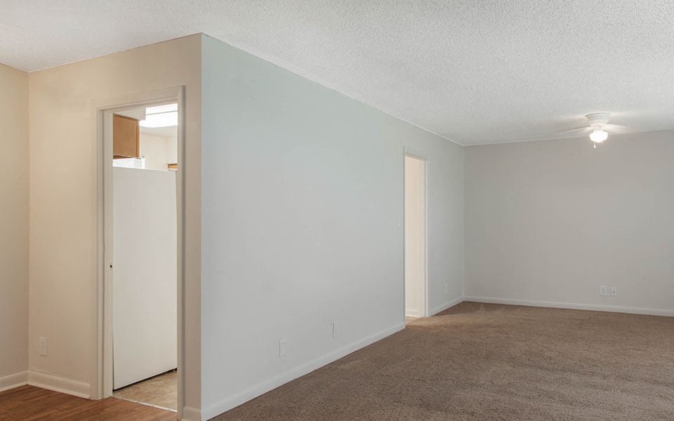 an empty living room with white walls and a white refrigerator