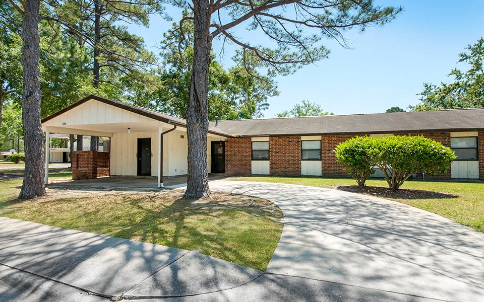 the front of a brick house with a driveway and trees