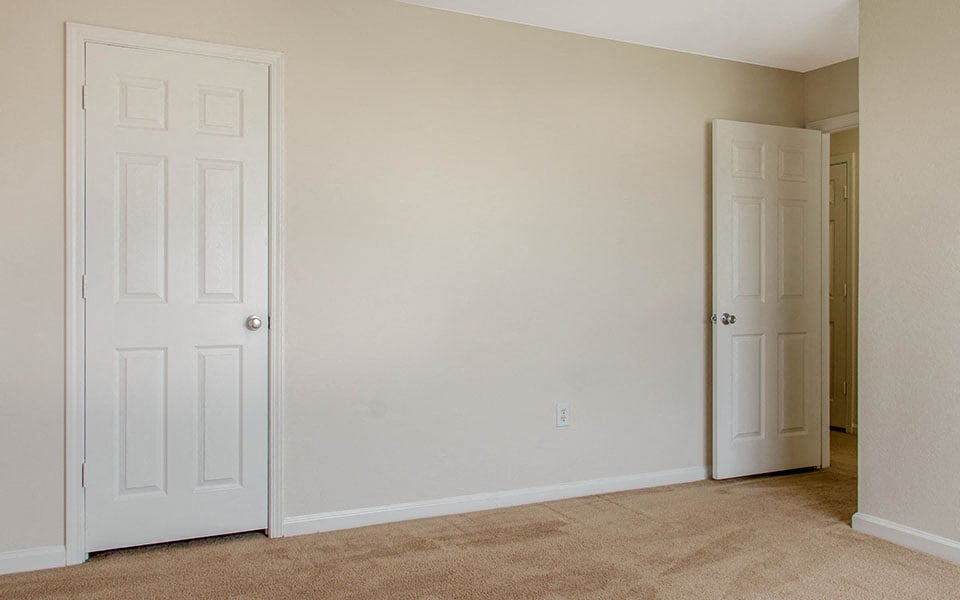 an empty bedroom with two doors and a closet