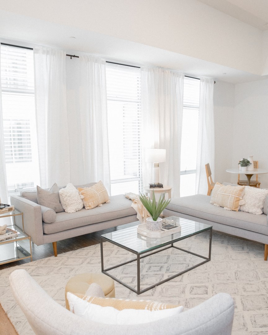 a living room with white curtains and couches and a coffee table