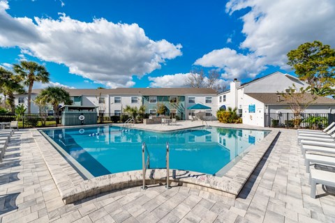A large outdoor swimming pool surrounded by lounge chairs and a building in the background.