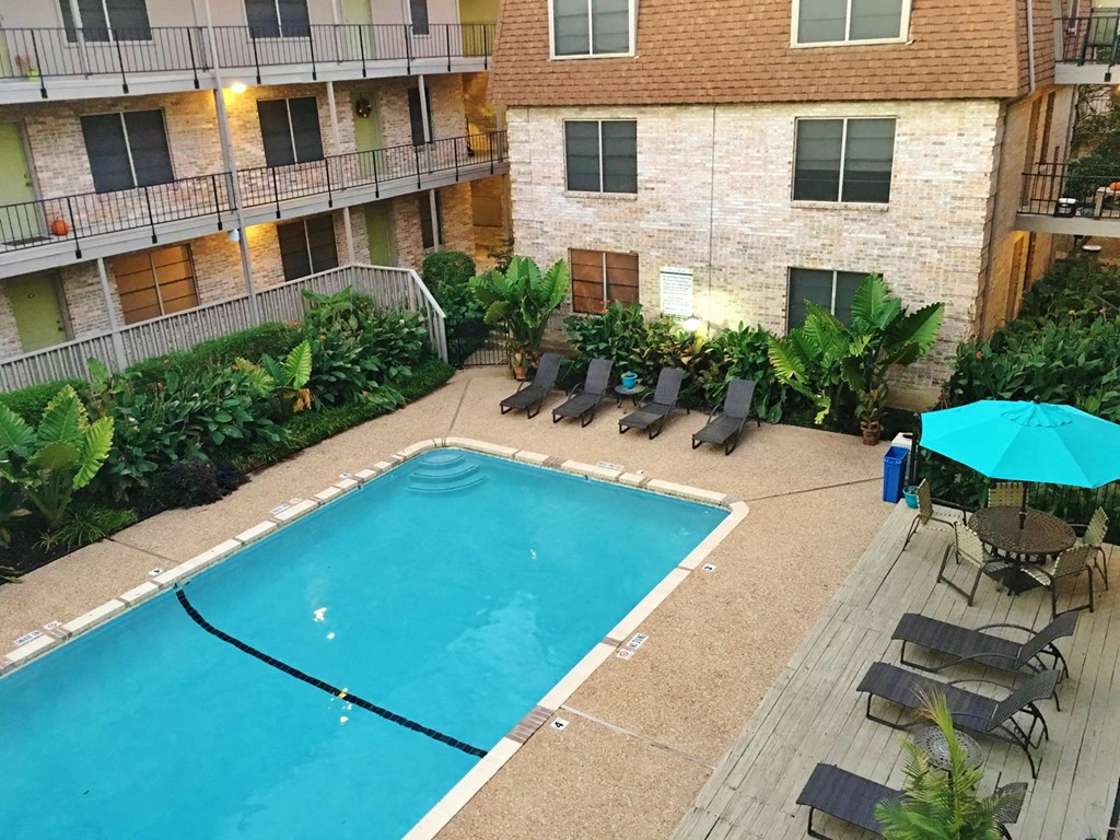 an outdoor pool with chairs and an umbrella in front of an apartment building