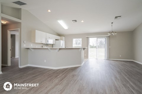 a spacious living room and kitchen with white cabinets and wood flooring