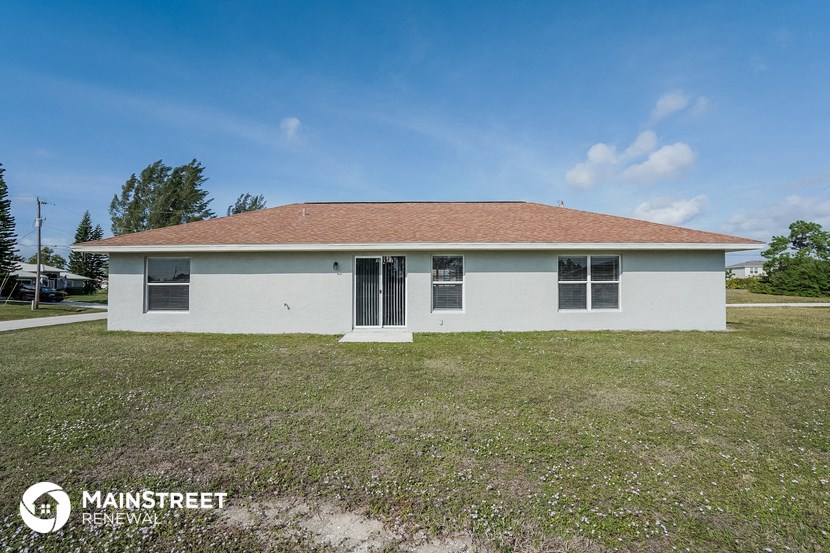 the front of a white house with a grass field