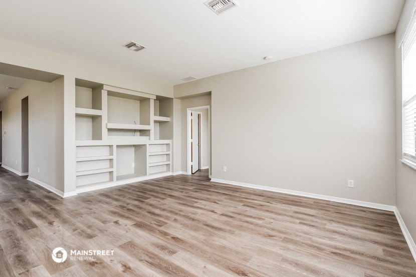 the spacious living room with white walls and wood flooring