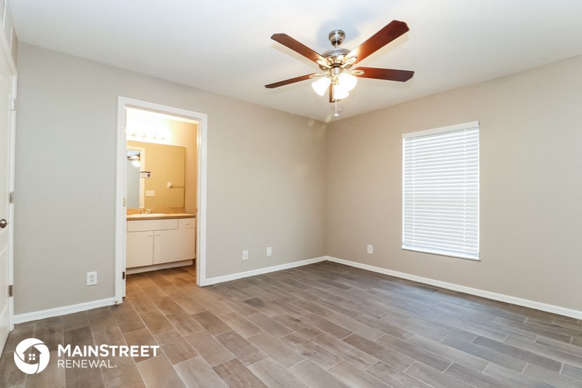 the spacious living room with wood flooring and a ceiling fan