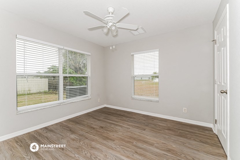 the living room of an empty house with a ceiling fan and two windows