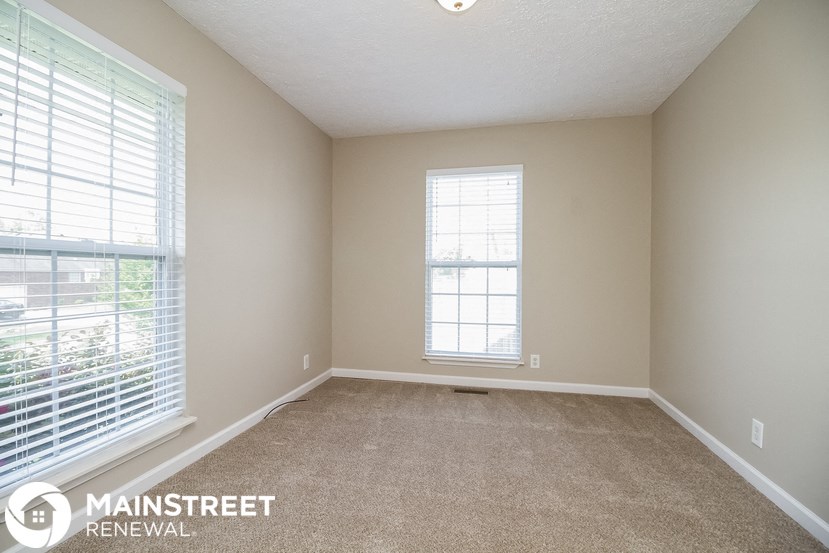 a spacious living room with two windows and a carpeted floor