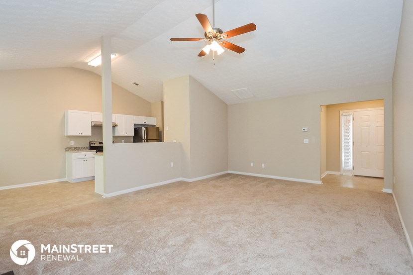 an empty living room with a ceiling fan and a kitchen