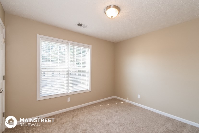 the spacious bedroom with a large window and carpeted flooring