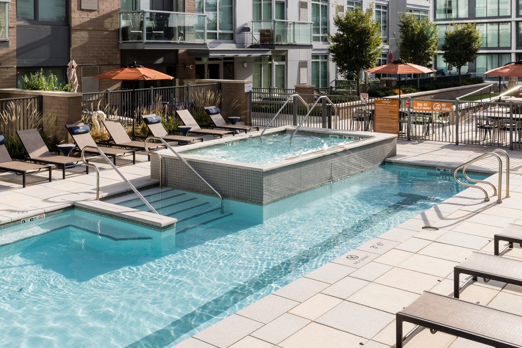 a swimming pool and spa with chairs and umbrellas in front of a building