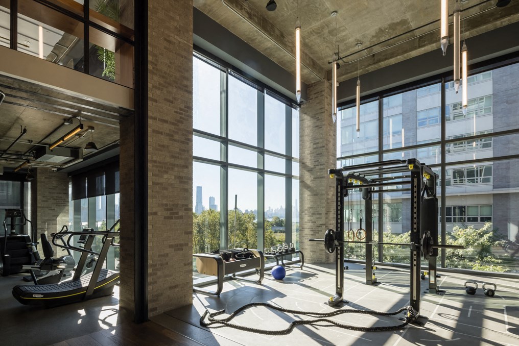 a workout room with tall windows and a view of the city