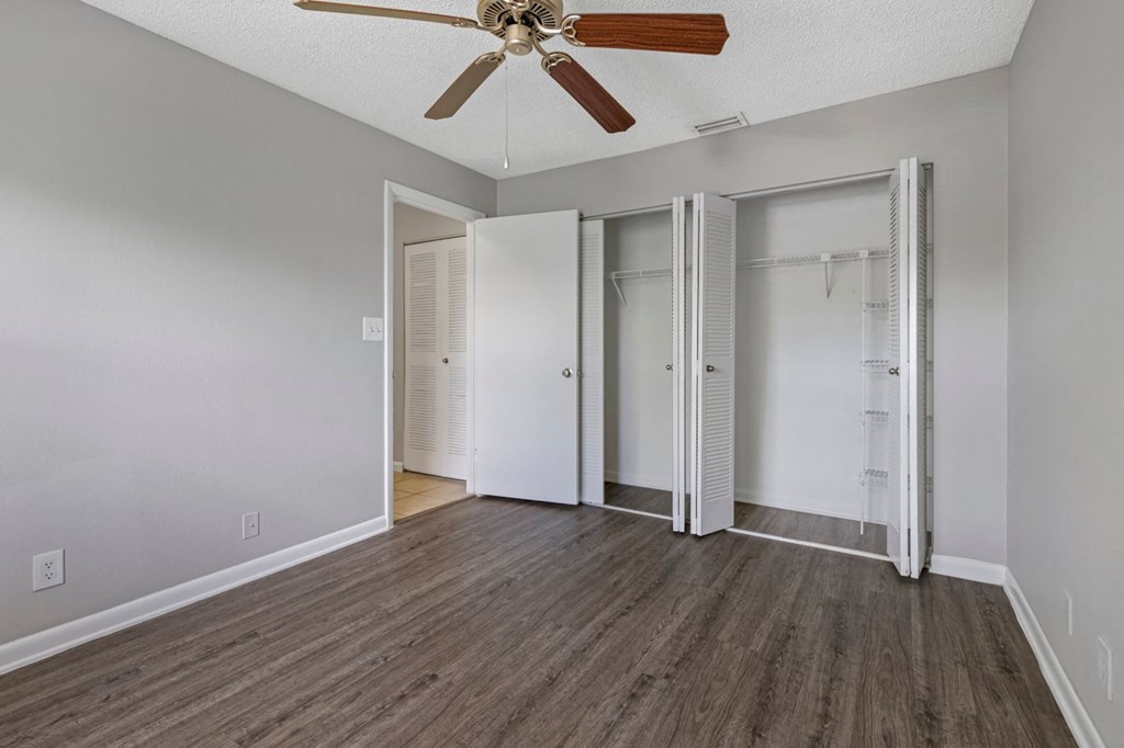 an empty living room with a ceiling fan and closets