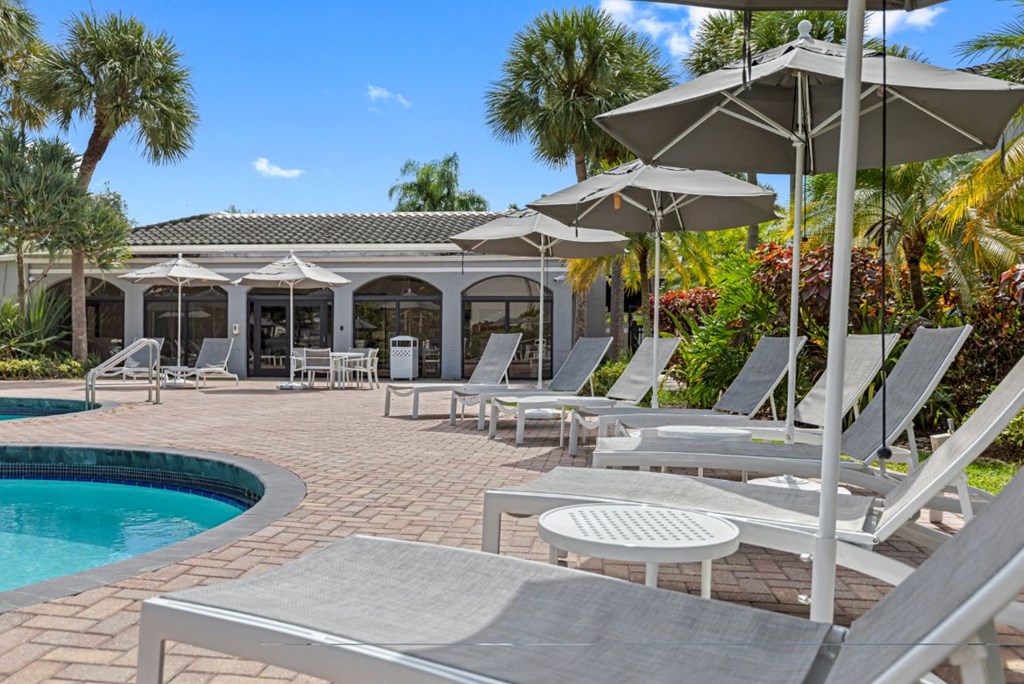 a patio with chairs and umbrellas next to a pool