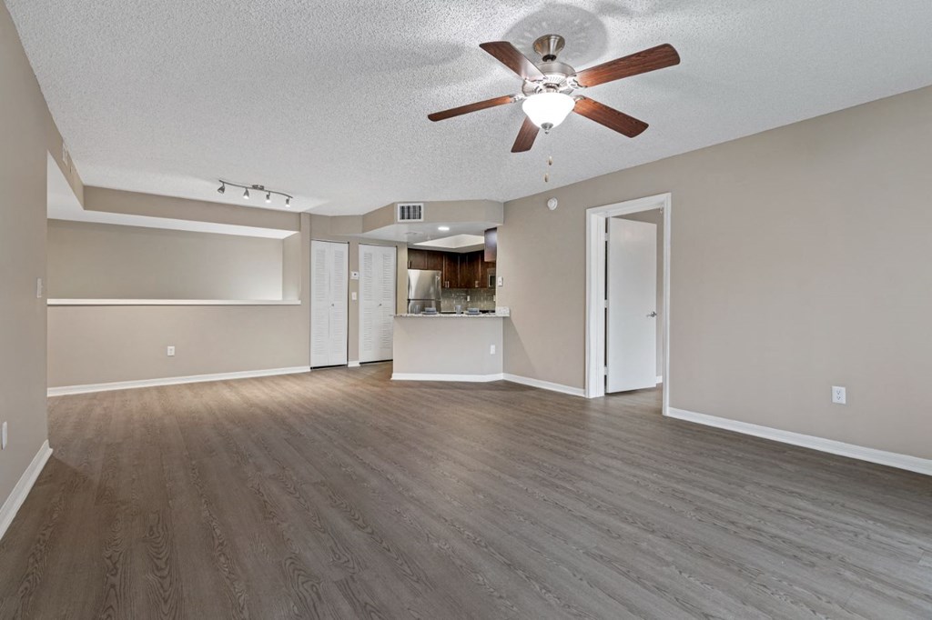 an empty living room with a ceiling fan and a kitchen