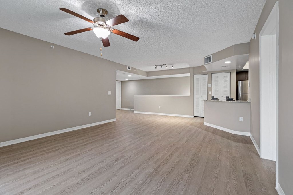 an empty living room with a ceiling fan and a kitchen