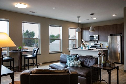 A modern living room with a brown leather couch and a kitchen area in the background.