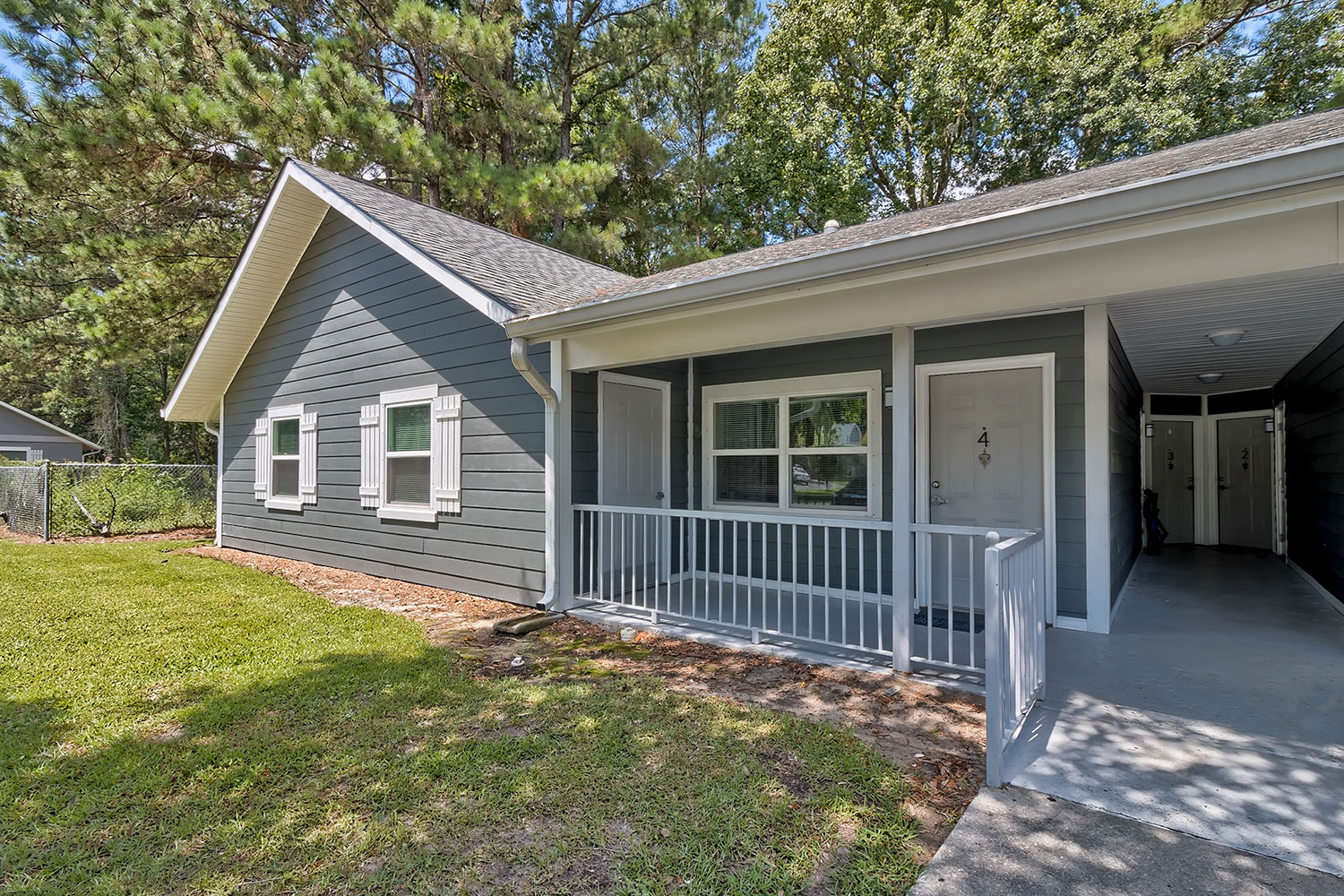 a small gray house with a porch and a green lawn