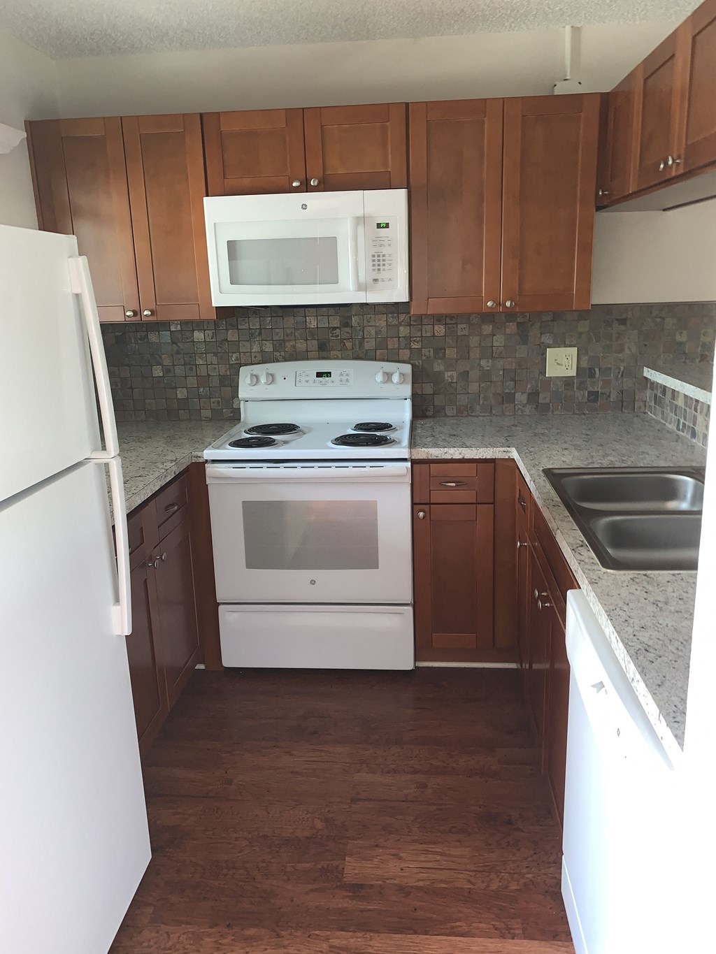 an empty kitchen with white appliances and wooden cabinets