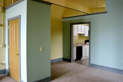 an empty living room with a kitchen in the background