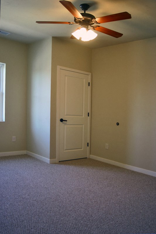 an empty living room with a ceiling fan and a door