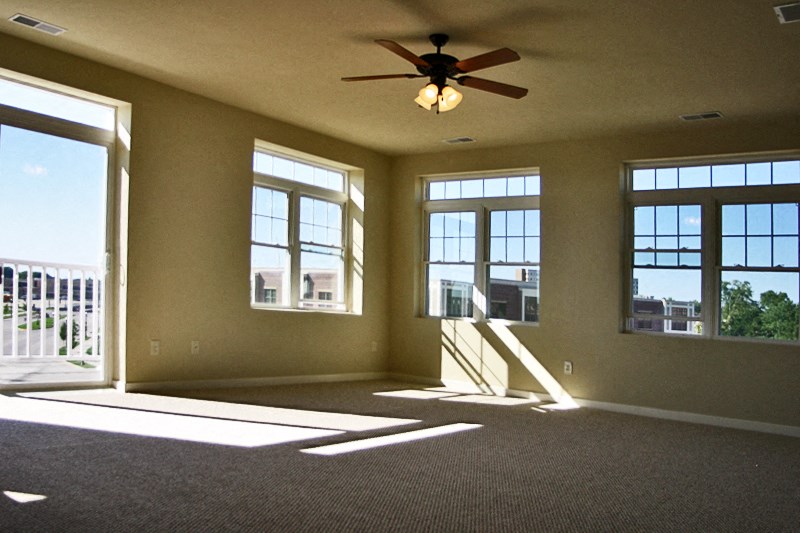 an empty living room with a ceiling fan and windows