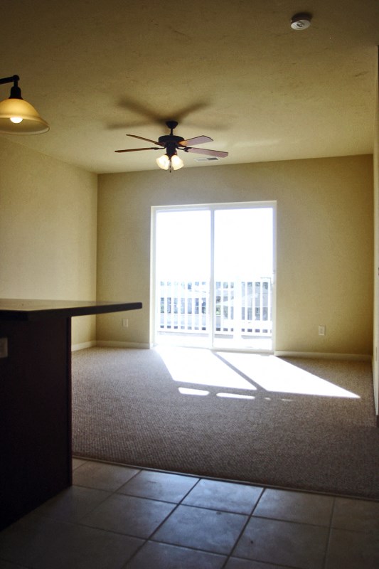 an empty living room with a ceiling fan and a balcony