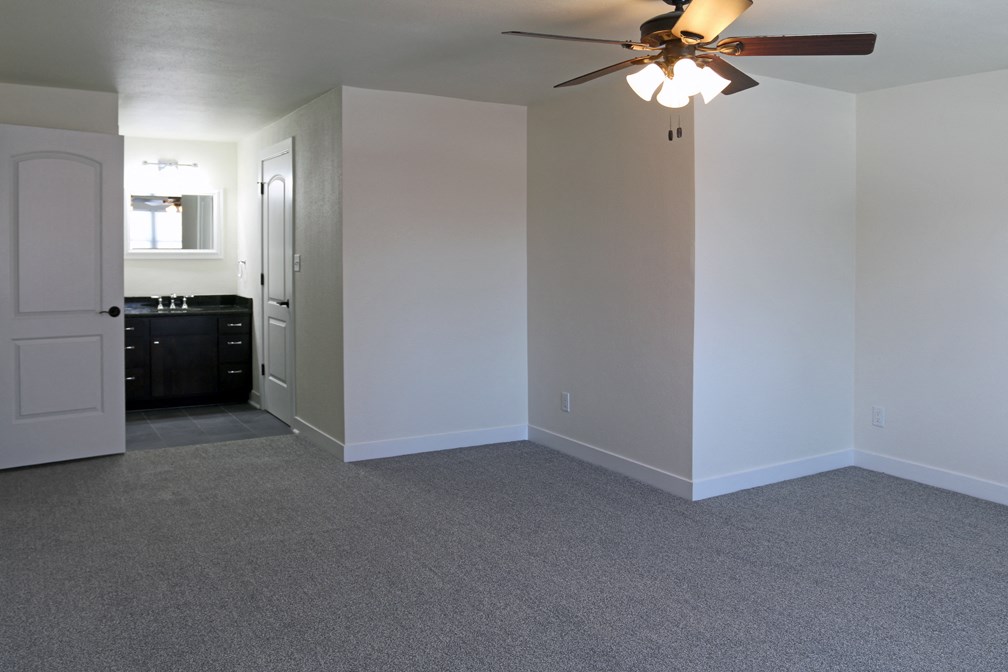 an empty living room with a ceiling fan and a kitchen