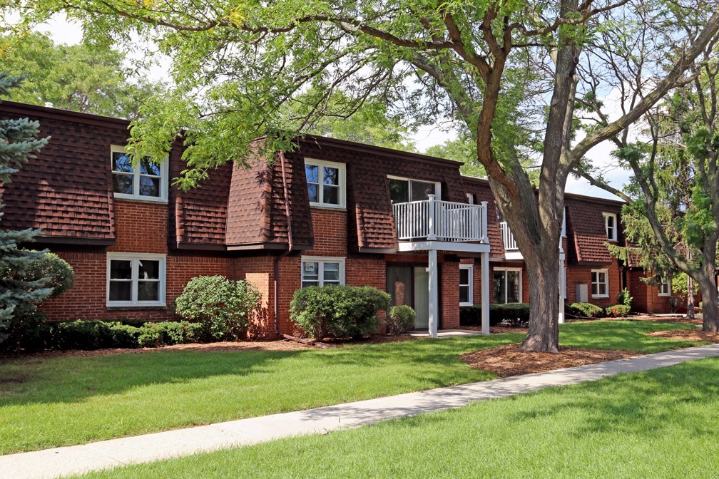 a red brick house with a porch and a tree in front of it