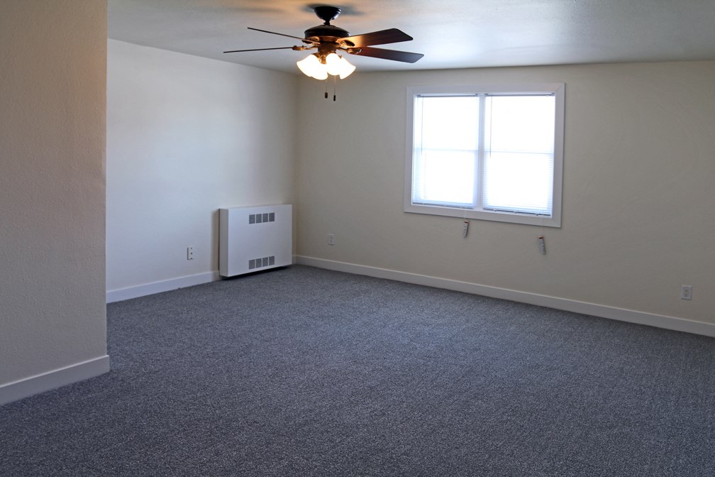 an empty living room with a ceiling fan and a window