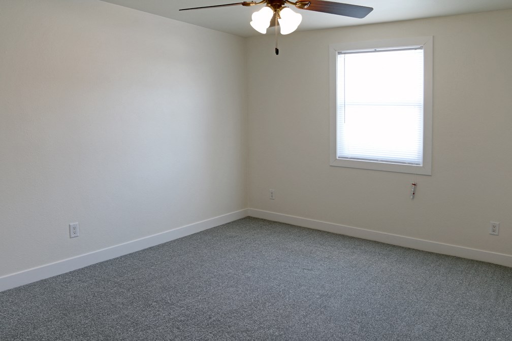 an empty bedroom with a ceiling fan and a window