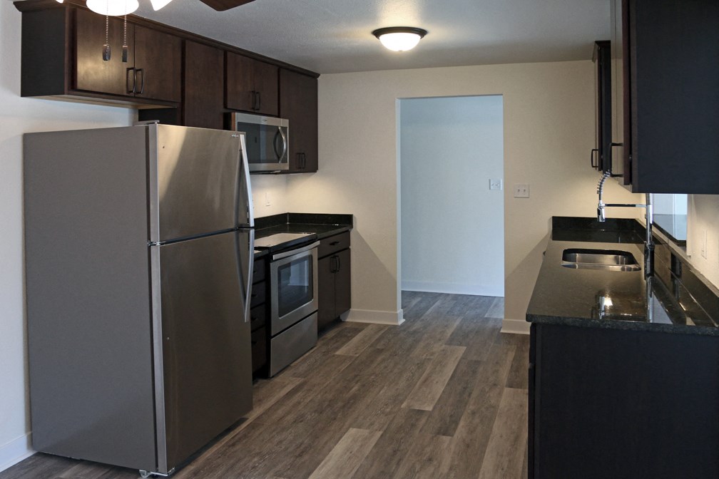 an empty kitchen with stainless steel appliances and wood flooring