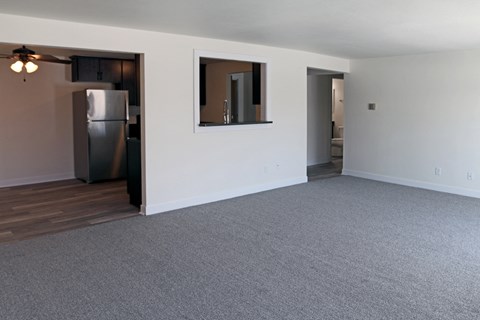an empty living room with grey carpet and a stainless steel refrigerator
